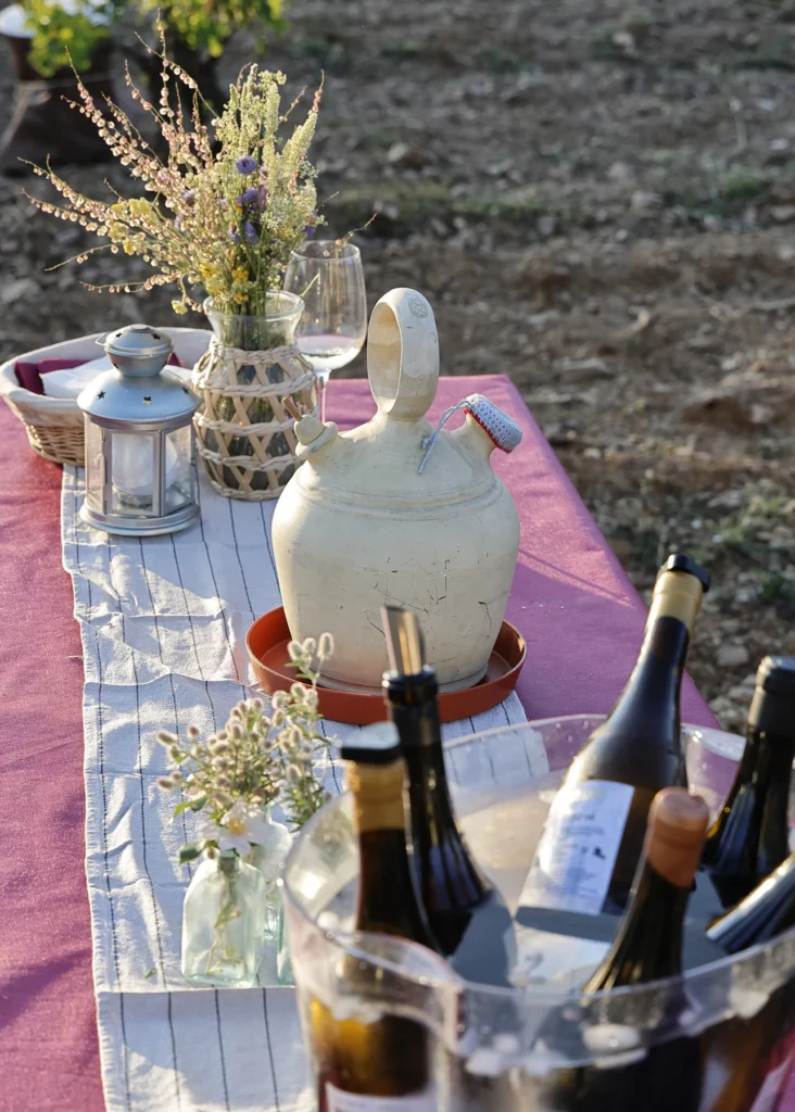 Mesa preparada con flores, copas y botellas de vino junto a las cepas